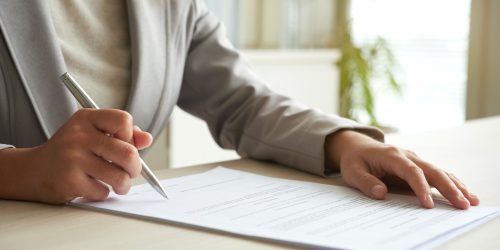 Hands of business entrepreneur signing document on her table